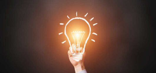 Human hand touching illuminated lightbulb on gray background.
